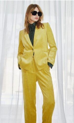 Una mujer vestida con un traje amarillo y gafas de sol con un toque de estilo americana de pana amarilla.