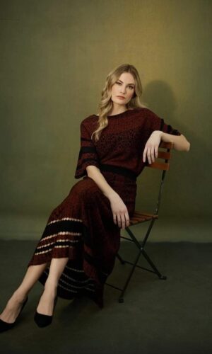 Una mujer sentada en un Top en punto en una silla con un vestido color burdeos.