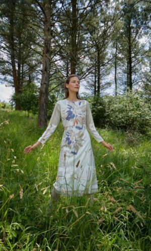Una mujer llamada Nicole, vestida con un Vestido Nicole beige, de pie en un campo de hierba.