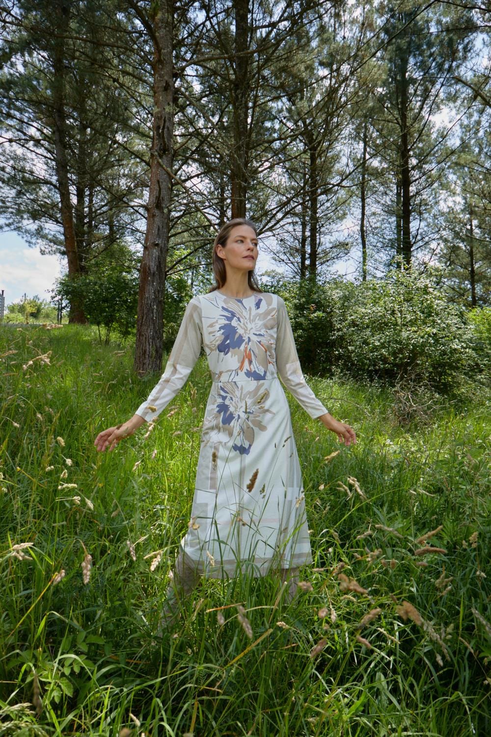 Una mujer llamada Nicole, vestida con un Vestido Nicole beige, de pie en un campo de hierba.