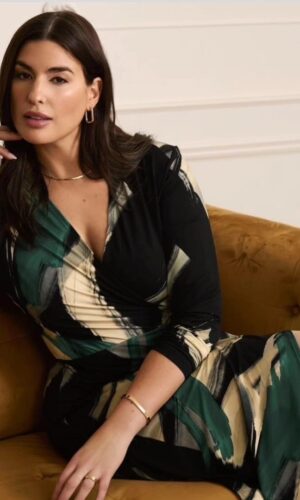 Una mujer está sentada en un sofá con un vestido cruzado manga larga con estampado abstracto en verde y negro.